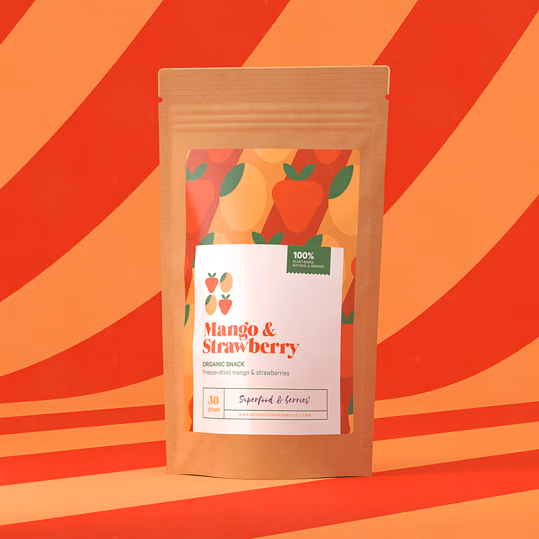 Ruskean paperipussin etiketissä teksti Mango & Strawberry, orgaaninen välipala, pakastekuivatut mango ja mansikat, värikkäällä taustalla mango- ja mansikkakuvioita.