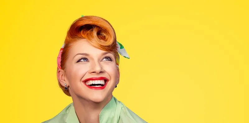Smiling retro-styled woman with red lipstick and vintage hairstyle against a bright yellow background.  
