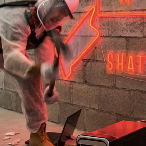 a person in a protective suit and face shield smashing an object with a sledgehammer