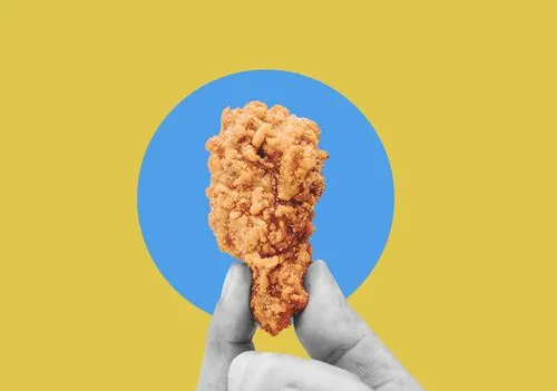Hand holding a crispy fried chicken strip on a colorful background.  
