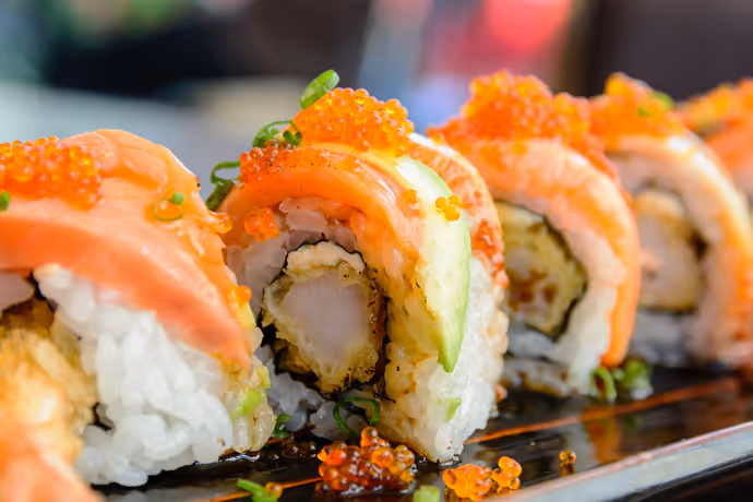 Close-up of fresh sushi rolls topped with salmon, avocado, and fish roe.  

