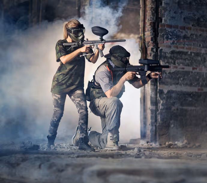 Two players in protective gear aiming paintball markers during an indoor paintball match.  
