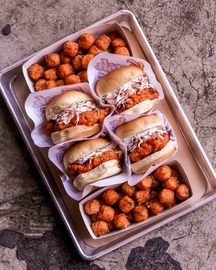Fried chicken sandwiches with coleslaw served with crispy tater tots on a tray.
