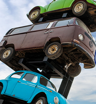 a quirky stack of three vintage cars, including a blue beetle and a brown vw van.