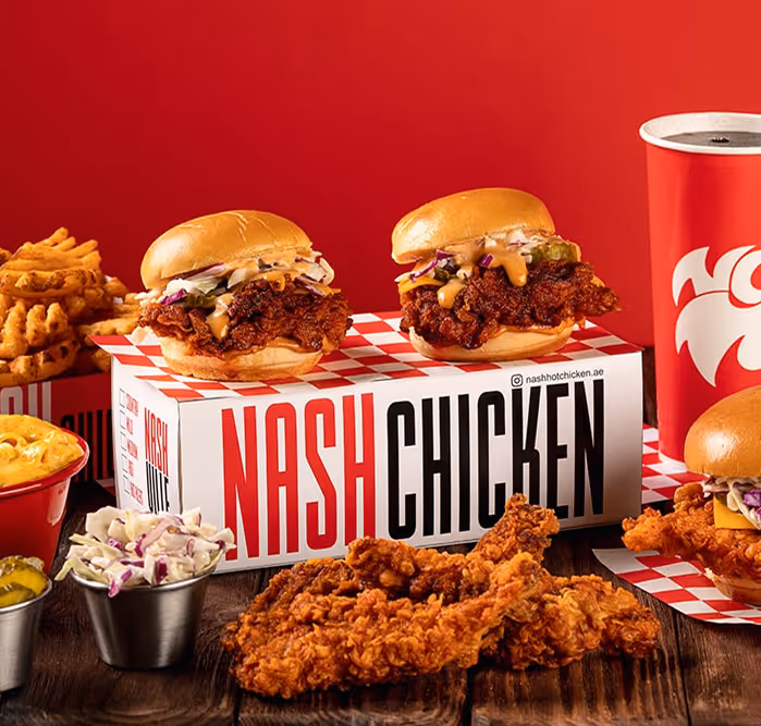 Delicious spread from Nash Chicken showcasing spicy chicken sandwiches, crispy fried chicken, waffle fries, mac and cheese, coleslaw, and a branded drink cup.