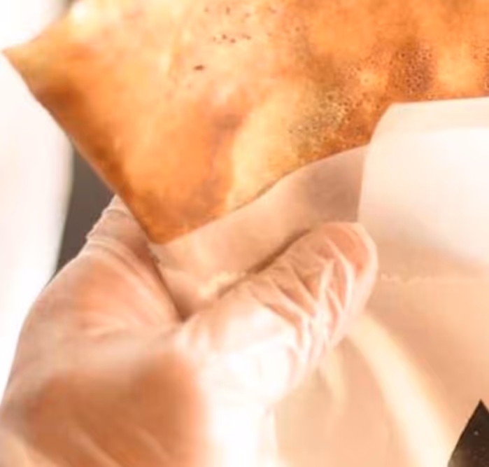 Close-up of a crispy golden-brown samosa held in a gloved hand with a paper wrapper.