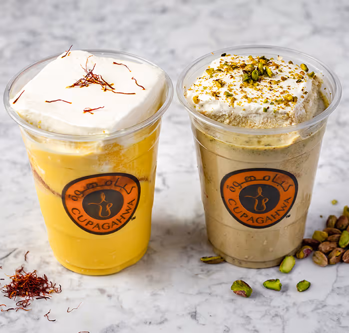 two-traditional-middle-eastern-drinks-in-clear-plastic-cups-with-the-cupagahwa-logo-one-saffron-flavored-with-cream-and-saffron-strands-the-other-pistachio-flavored-topped-with-whipped-cream-and-chopped-pistachios