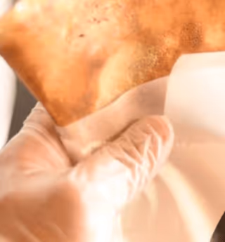 gloved hand holding a crispy, golden-brown folded pastry in white paper