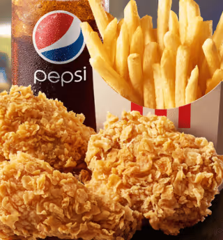 close-up of crispy fried chicken pieces, french fries in a box, and a pepsi drink