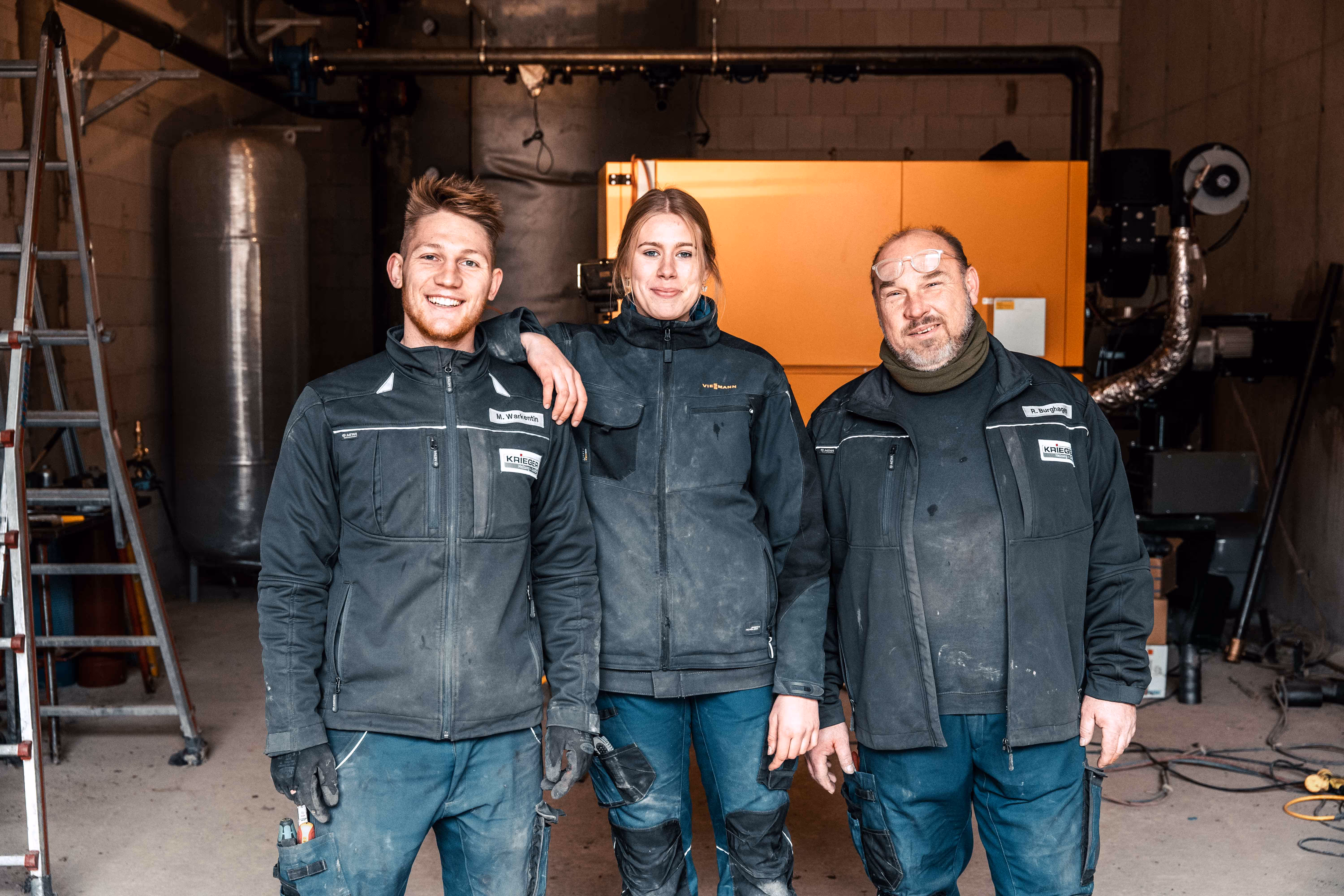 Drei Krieger Mitarbeiter in Arbeitskleidung lächeln in die Kamera.