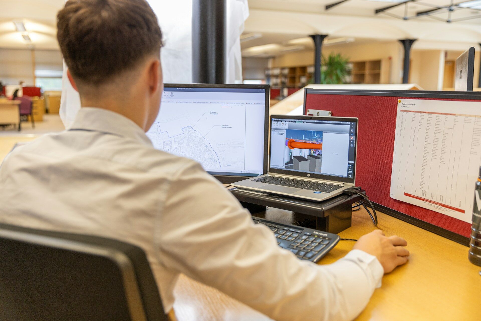 Person standing at desk in front of two screens