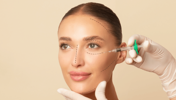 Woman receiving cosmetic injection in cheek with marked lines on face, held by gloved hands.