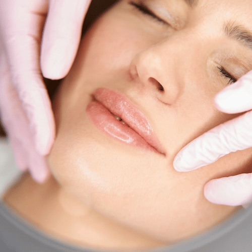 Close-up of a woman's face with closed eyes as a person wearing pink gloves gently touches her cheeks.