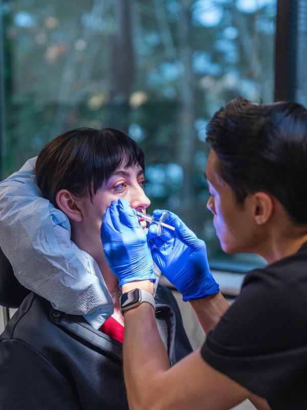 Medical professional wearing blue gloves administering a lip injection to a seated woman in a clinical setting.