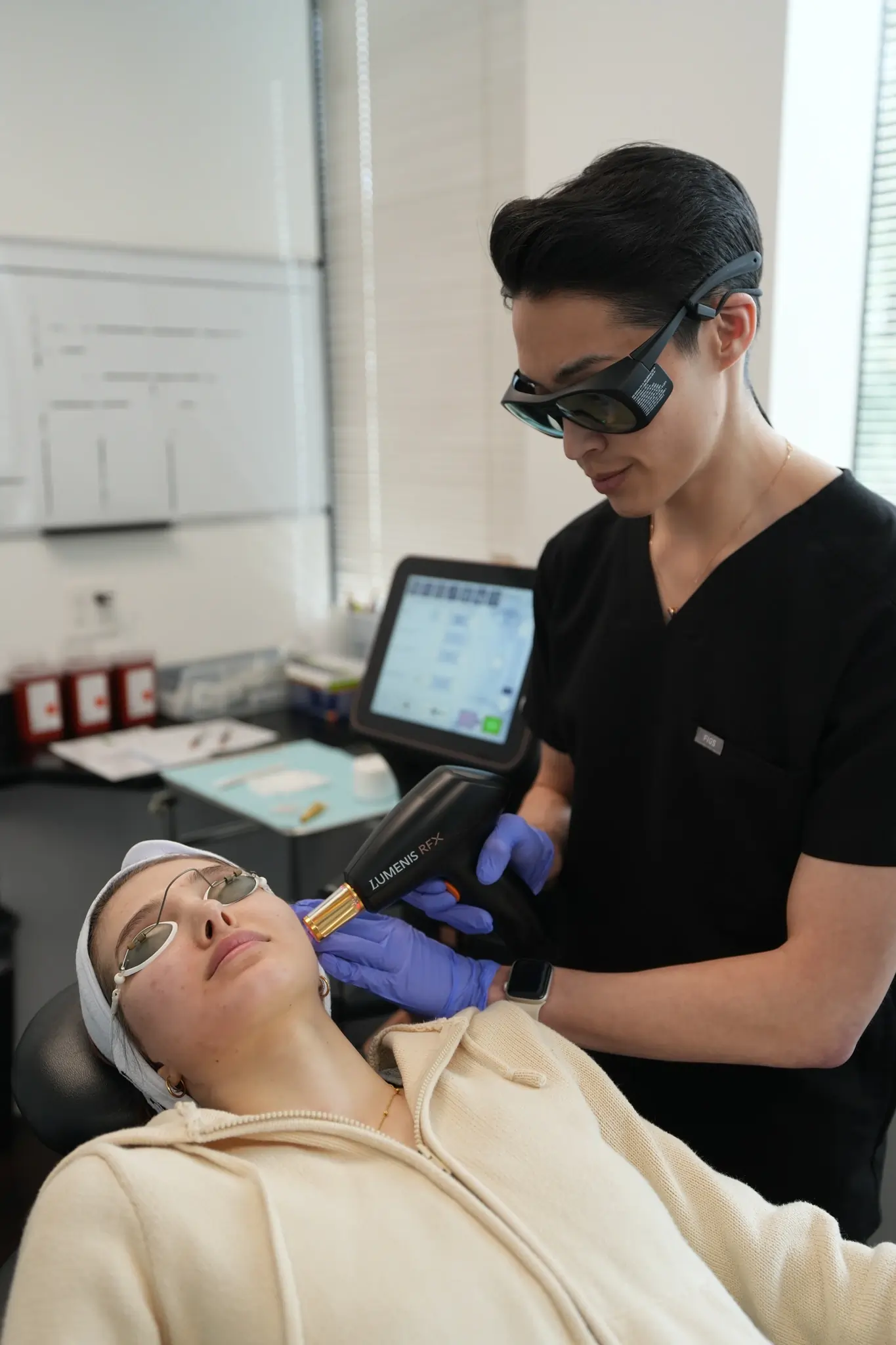 Woman receiving a facial treatment with a handheld device from a professional wearing gloves in a spa setting.