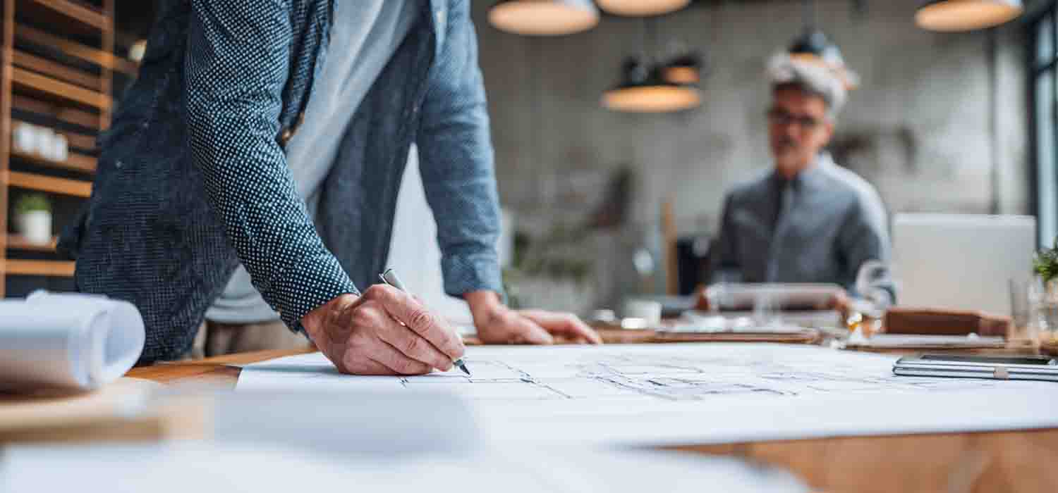 IT consultant walking a small business owner through a printed dossier d’architecture on a meeting table