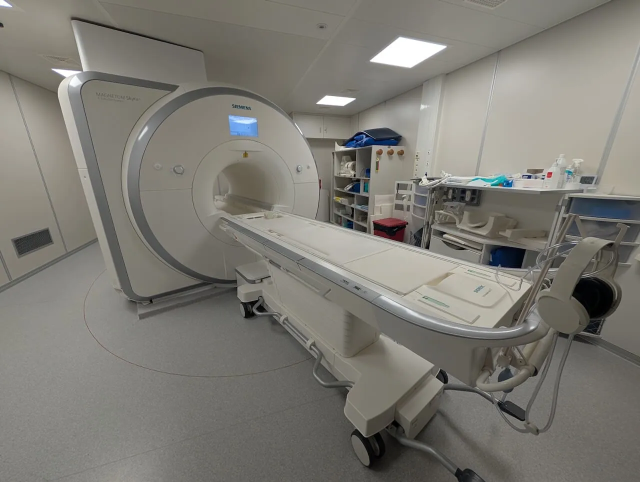 SIEMENS MAGNETOM Skyra MRI scanner machine in a medical room with patient table and headphones attached.