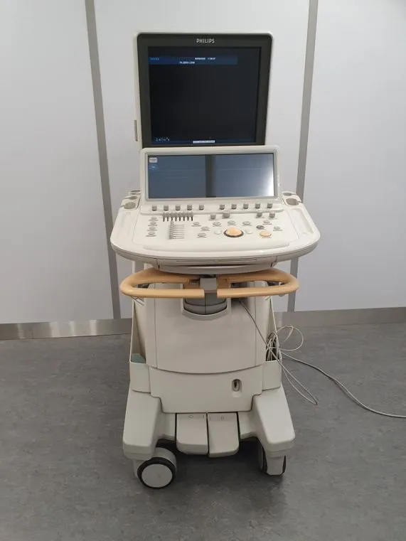 Philips medical ultrasound machine with dual monitors and control panel on wheels in a clinical room.