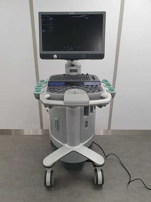Siemens ultrasound machine with monitor, keyboard, control panel, and multiple probe holders on wheels in a medical room.