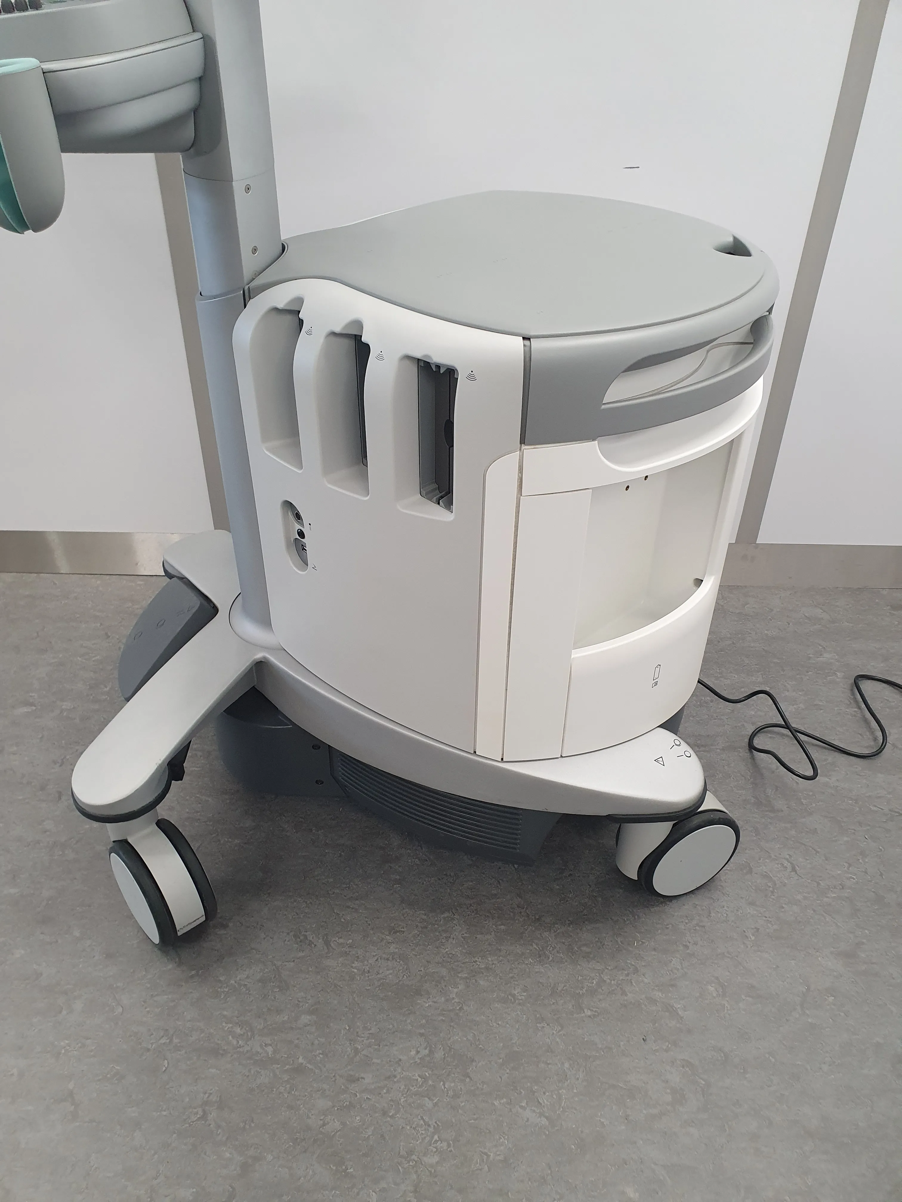 Close-up of a medical device base with wheels on a gray floor in a clinical setting.