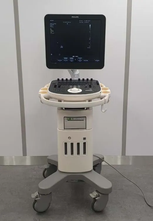 Philips ultrasound machine with screen, control panel, and wheeled base in a clinical room.