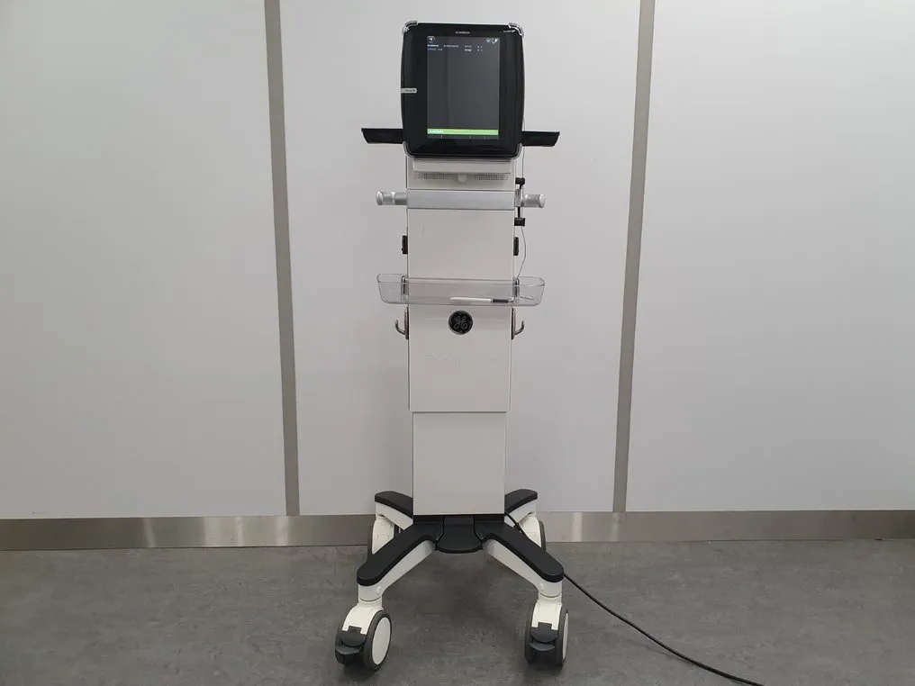 Medical device on wheels with a screen and control panel, standing in a room with plain walls.