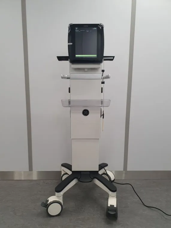 Mobile medical ventilator device with digital screen on a wheeled stand in a clinical setting.