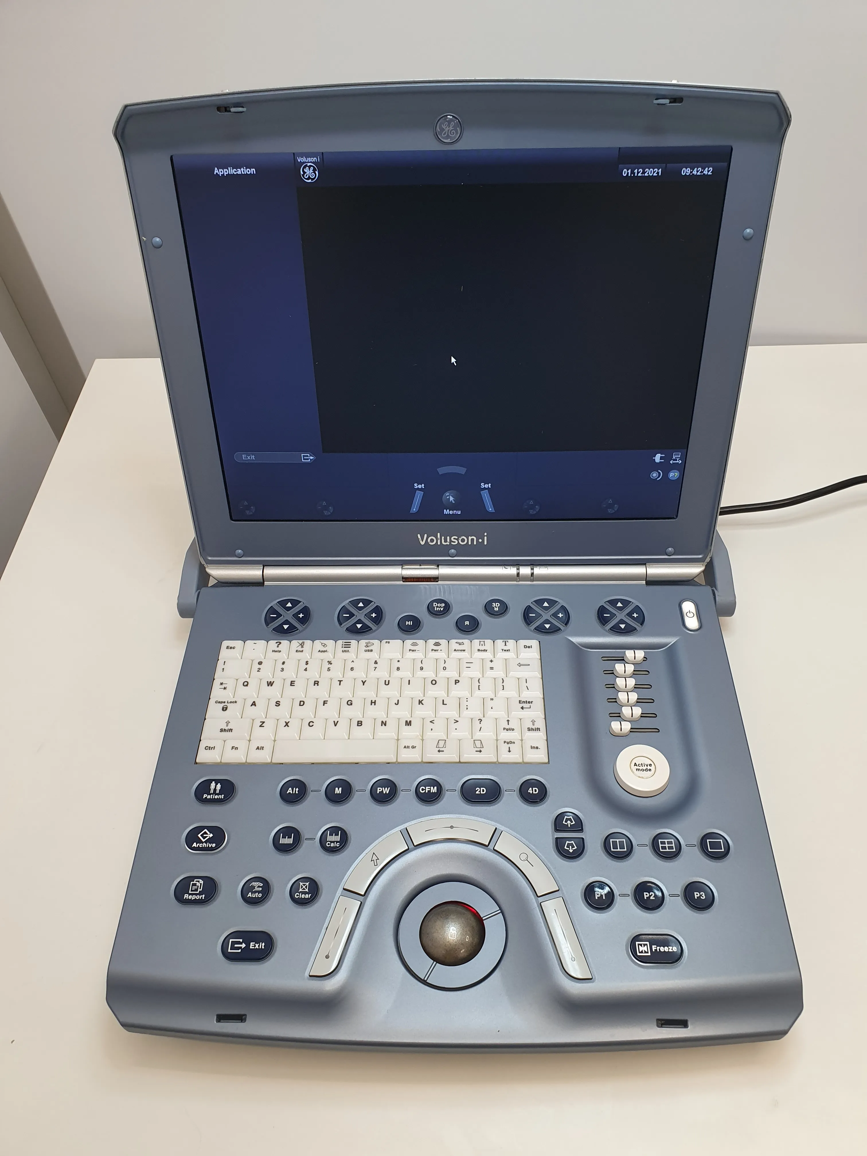 GE Voluson i portable ultrasound machine with screen, keyboard, control buttons, and trackball on a white table.