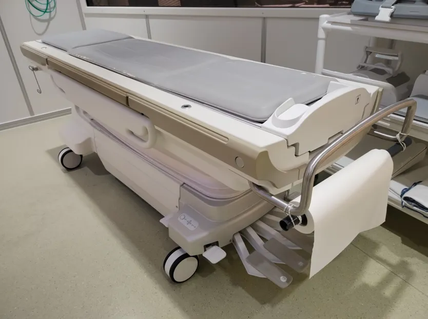 Modern medical examination table with wheels, padded surface, and a paper roll holder.