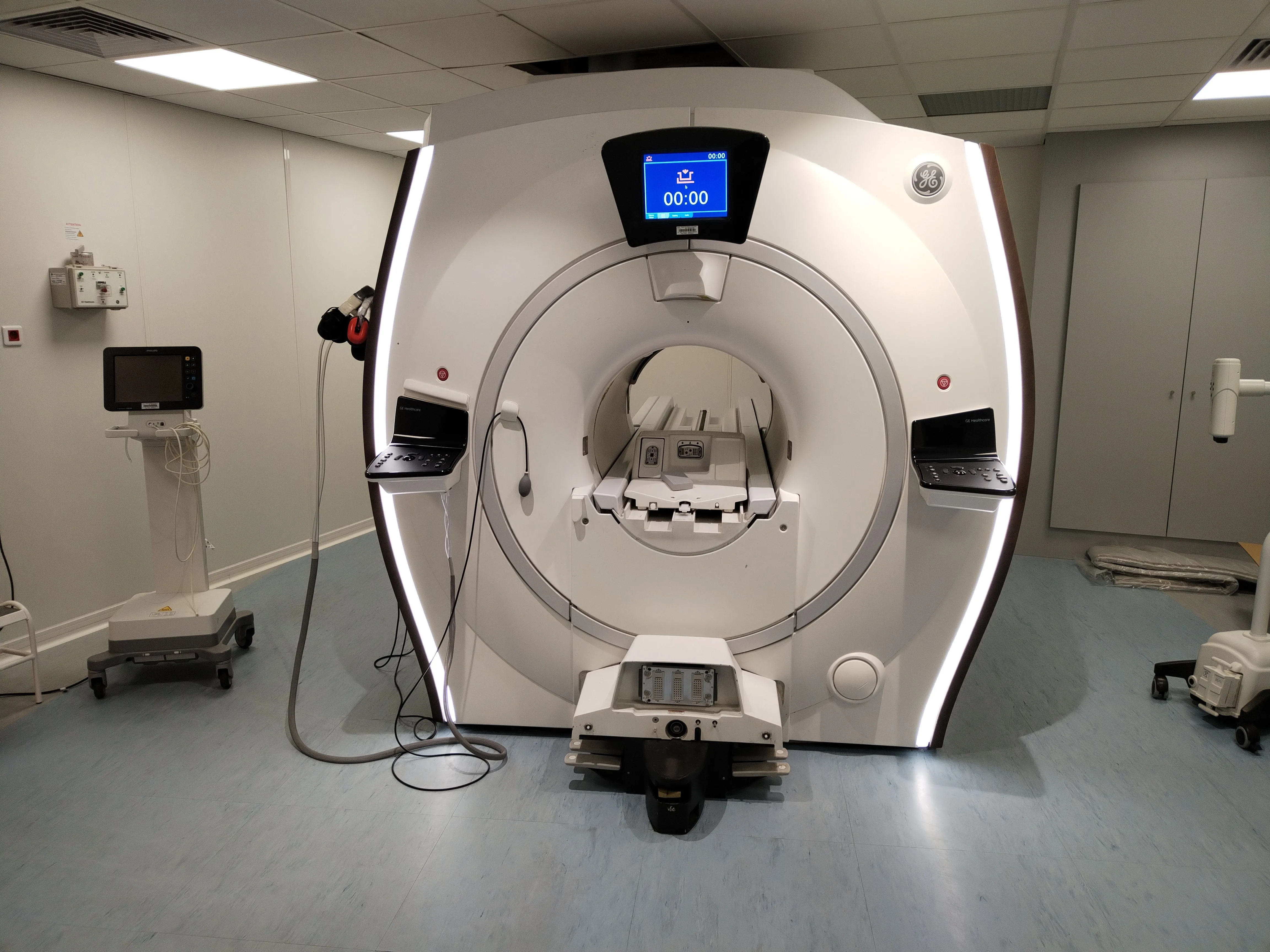 Modern GE Healthcare MRI machine in a clinical room with clean, white walls and blue flooring.