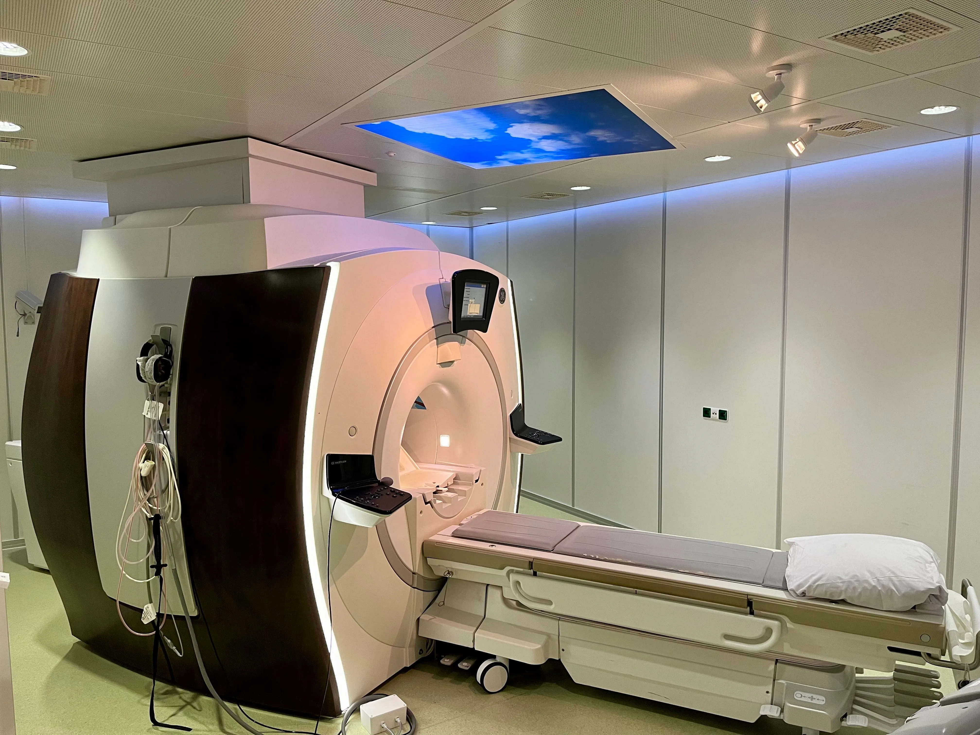 Modern MRI machine in a medical imaging room with a patient table and ceiling panel displaying a sky image.