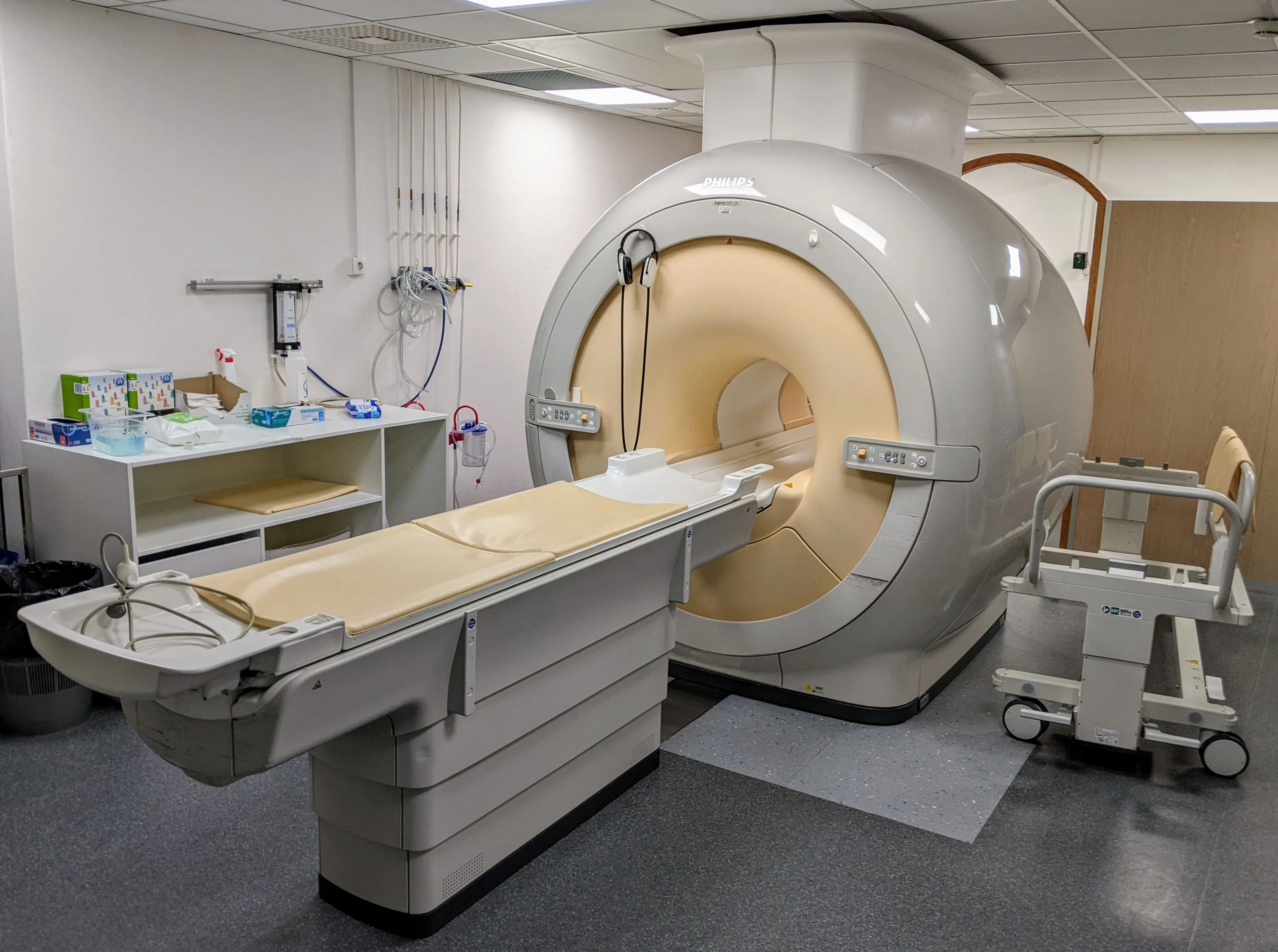 Philips MRI machine in a clinical room with a beige padded patient table and medical supplies on a countertop.