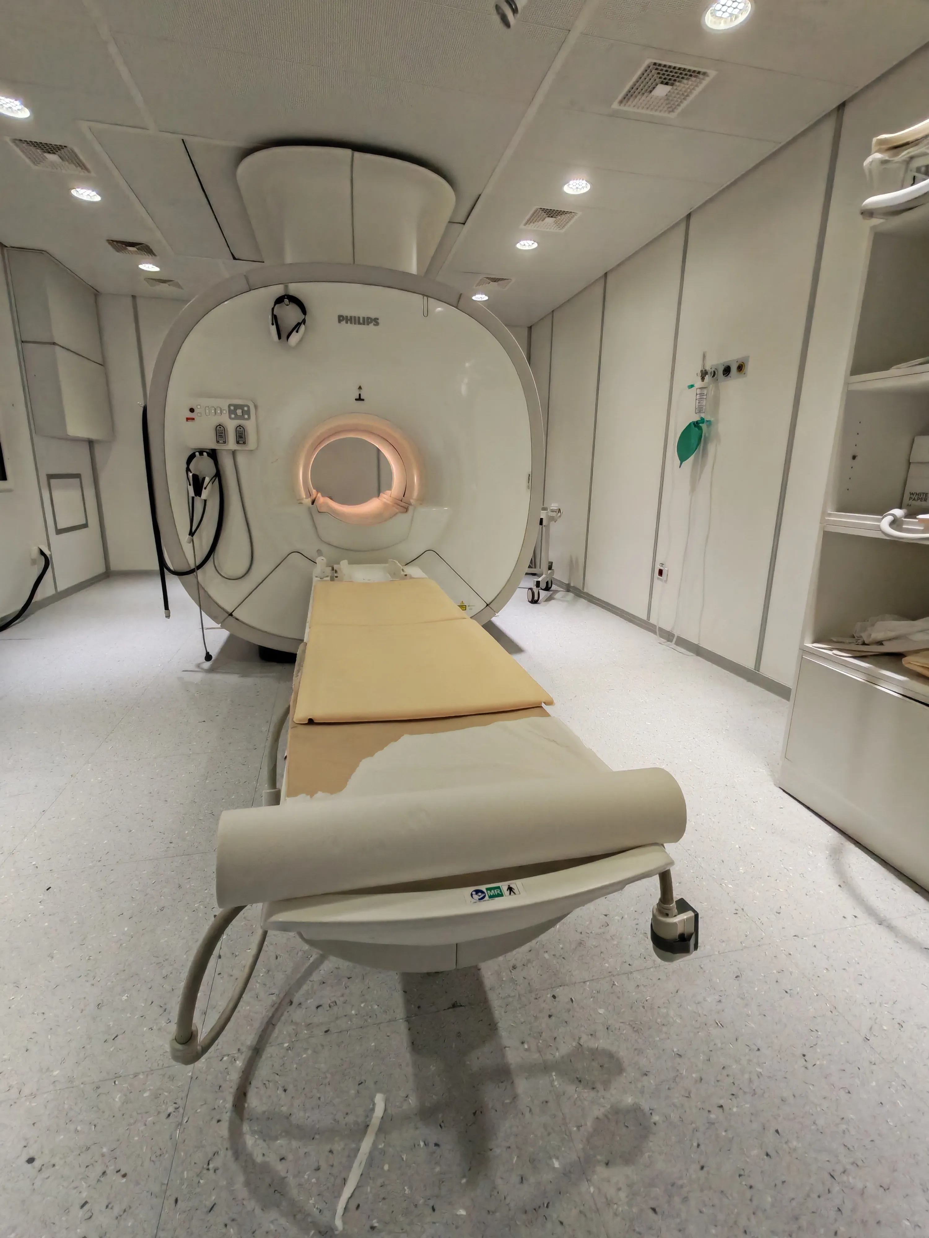 MRI scanner machine with patient table covered in paper sheet inside a clean medical room.