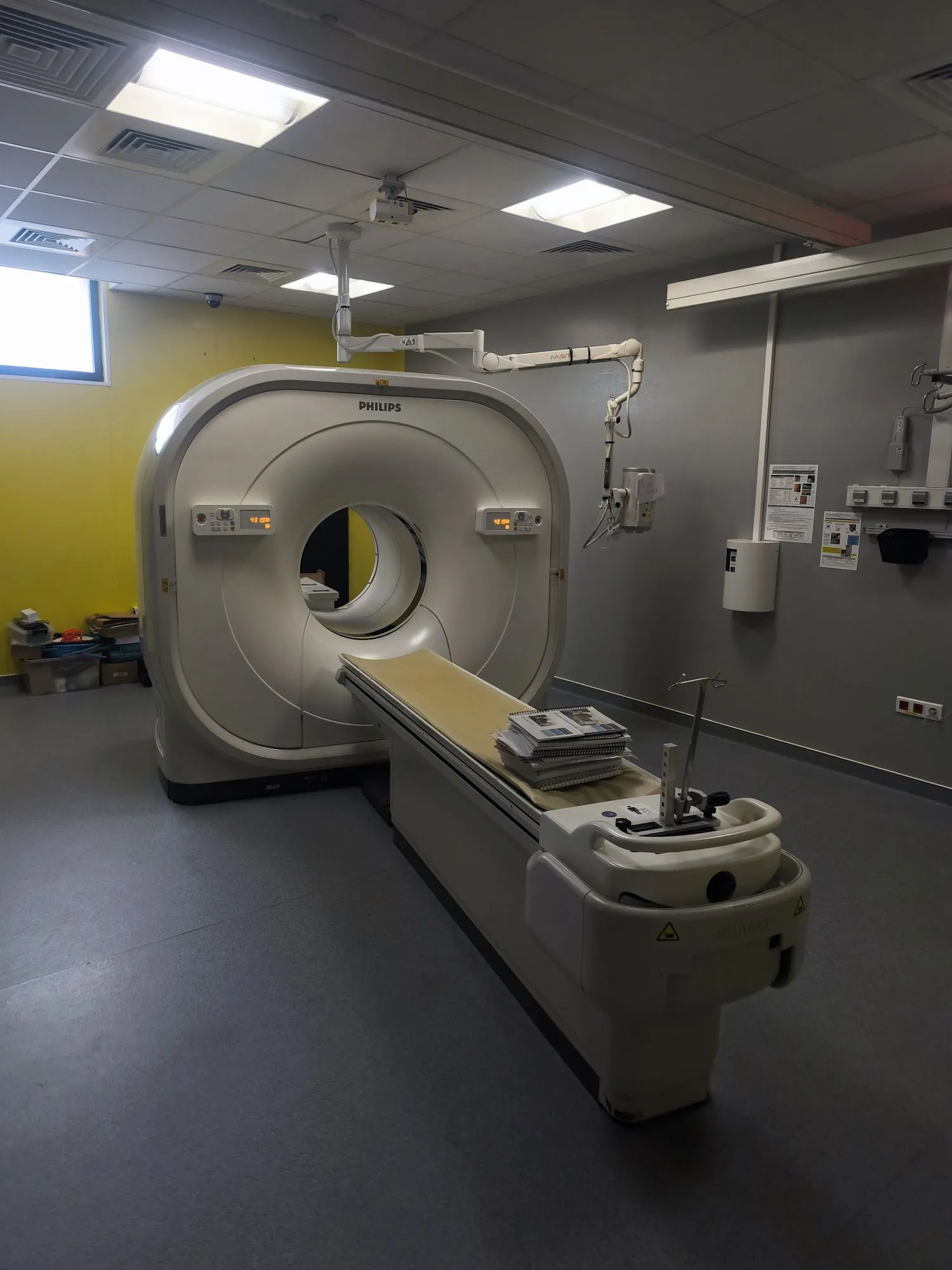 Philips CT scanner machine in a medical imaging room with patient table covered by documents.