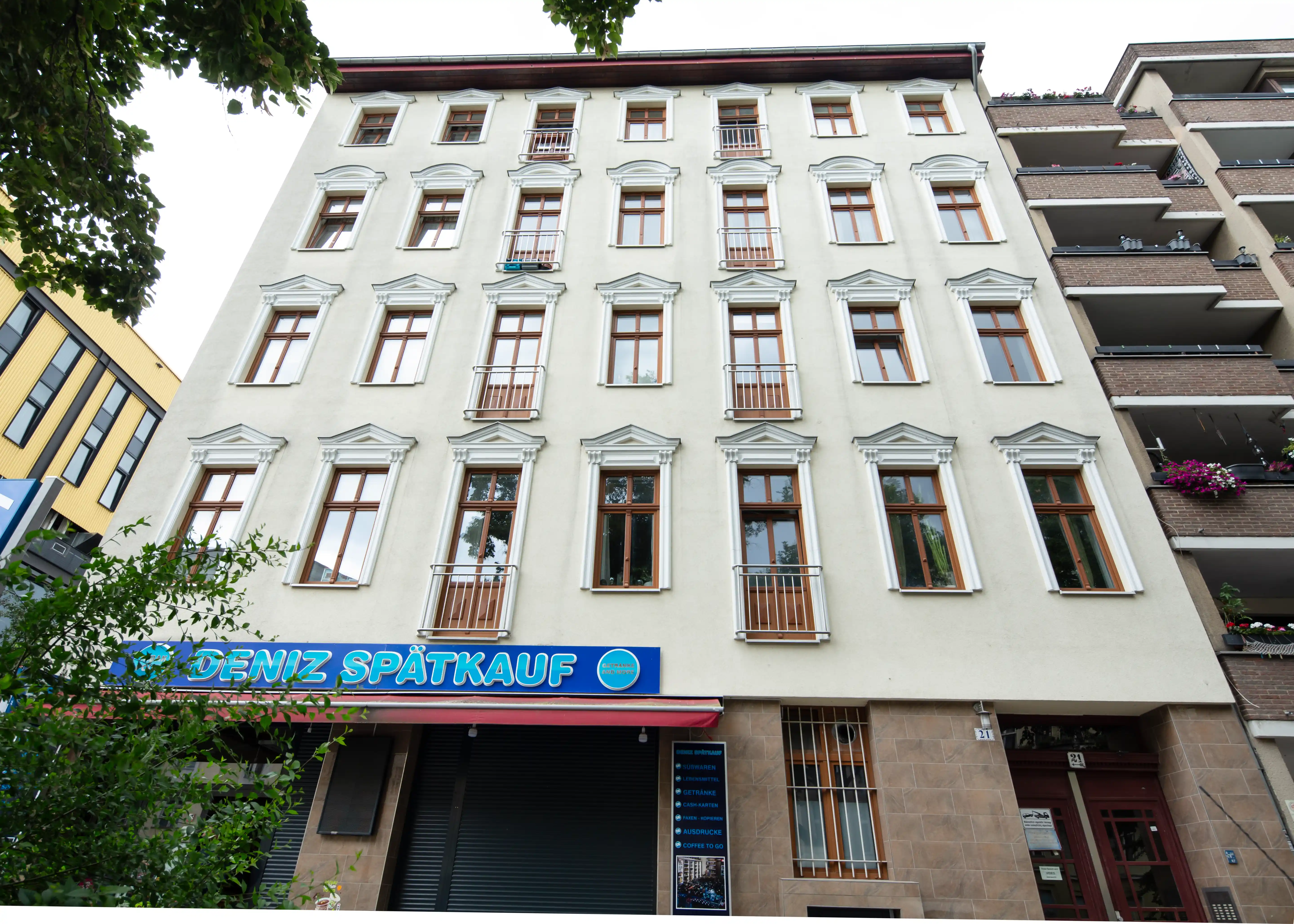 Mehrstöckiges Wohngebäude mit vielen Fenstern, darunter ein Geschäft mit der Aufschrift 'Deniz Spätkauf'.