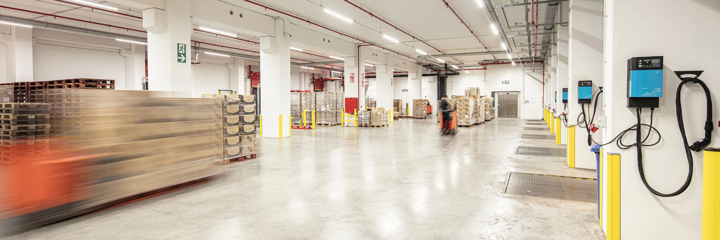 Wide warehouse interior with pallets stacked and a person operating a forklift in motion.