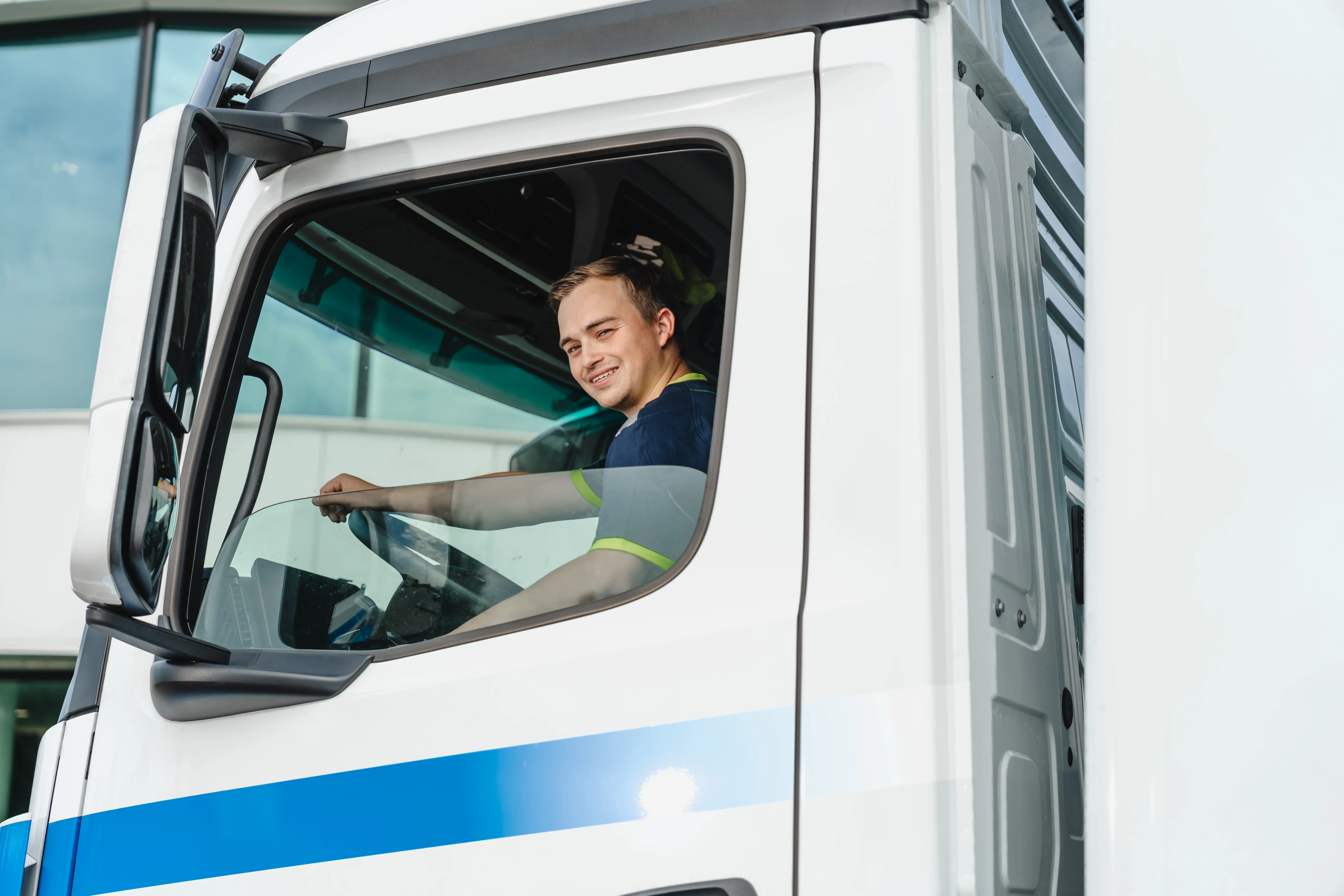 Smiling young man sitting in the driver seat of a white truck with a blue stripe.