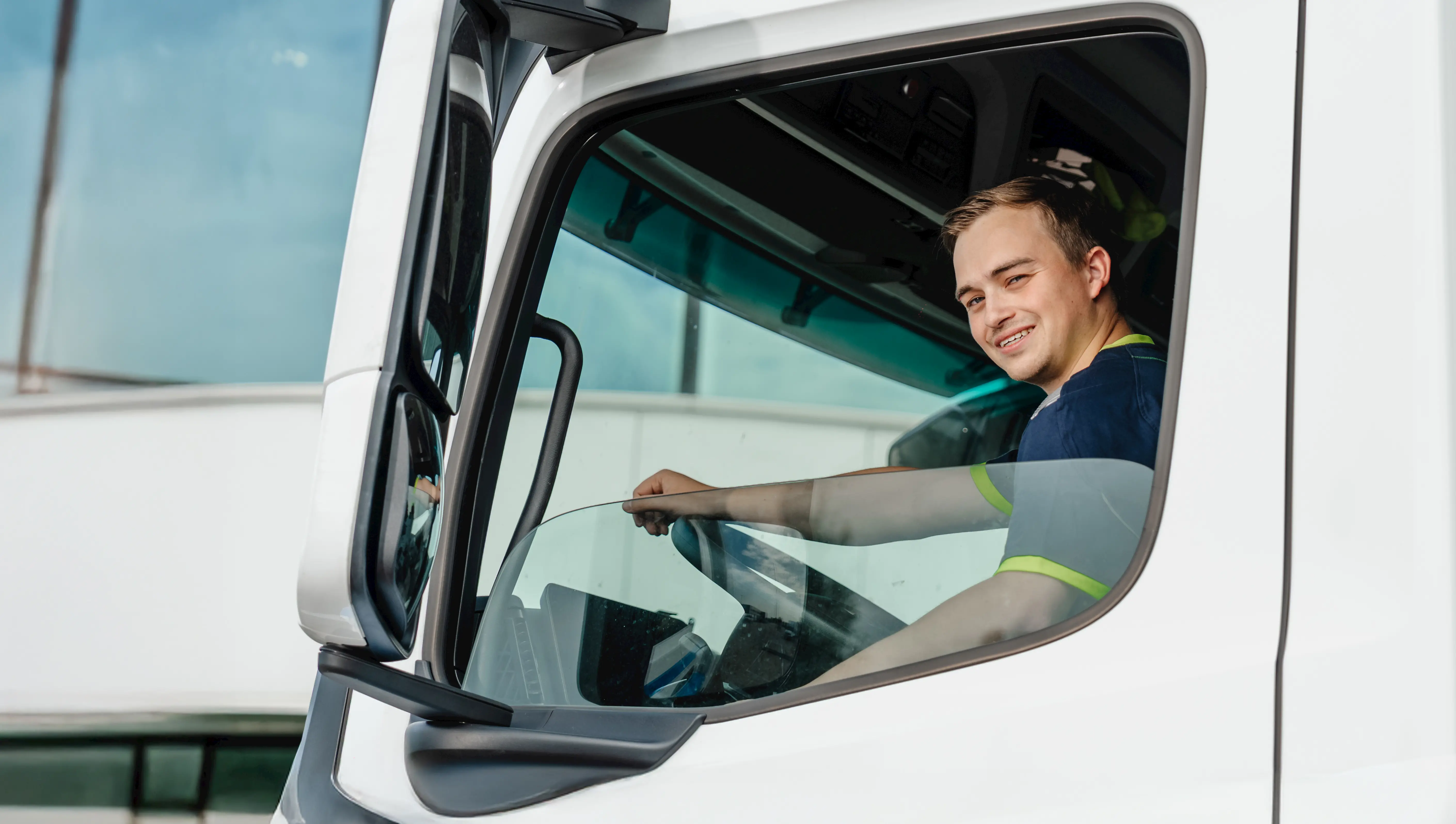 Smiling young man sitting in the driver's seat of a white truck looking out the window.