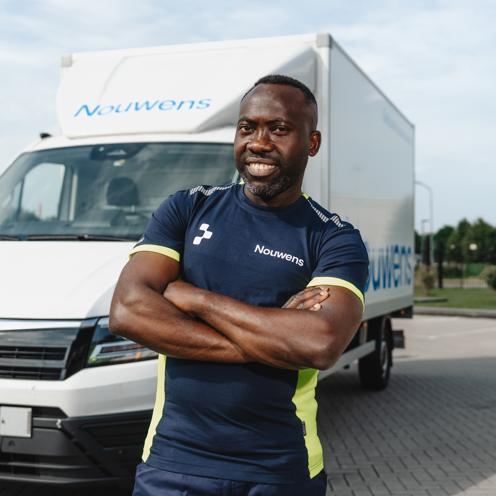 Smiling man in Nouwens uniform with arms crossed standing in front of a Nouwens delivery truck.