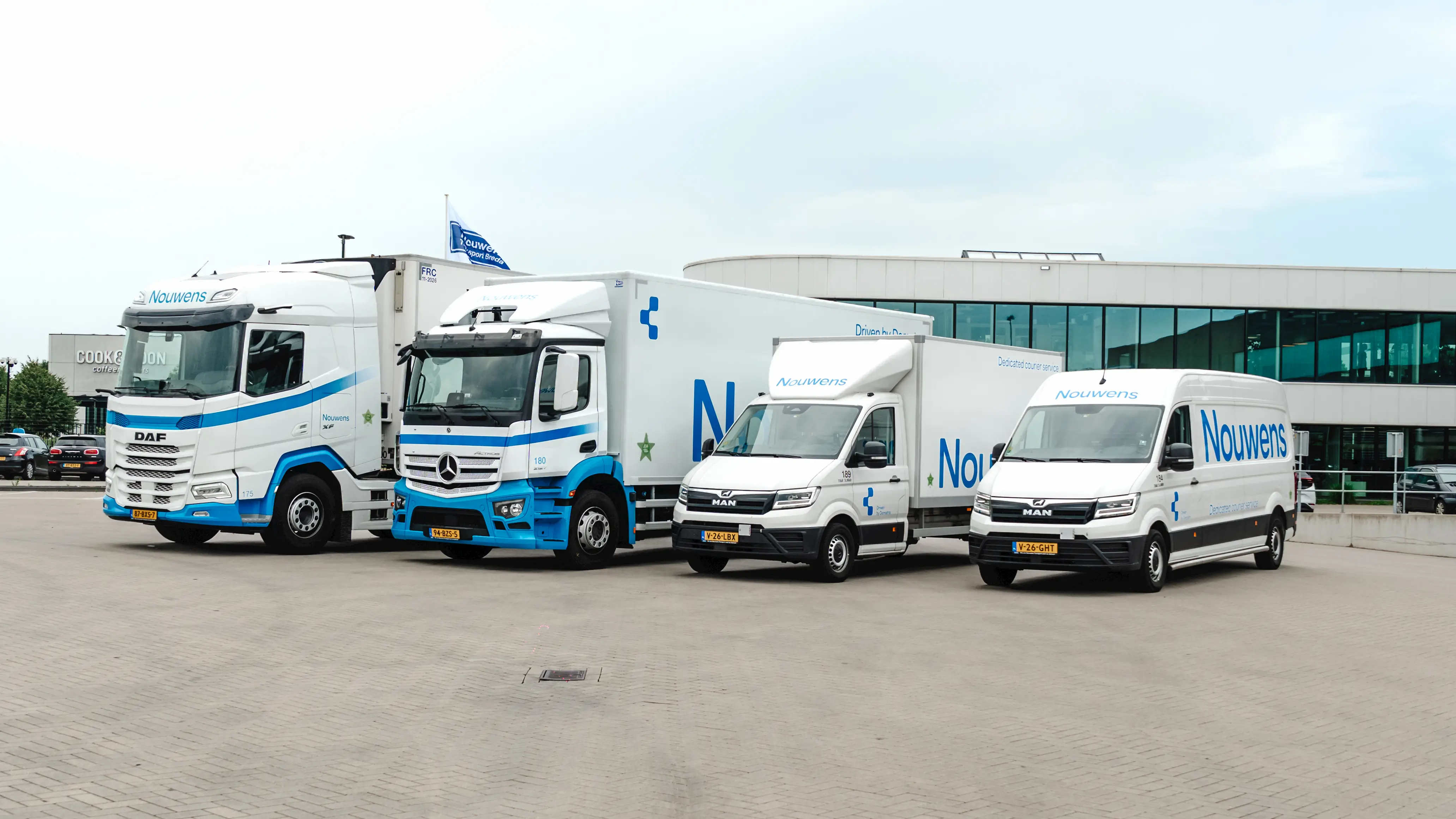 Four white and blue delivery trucks and vans with Nouwens branding parked in front of a modern glass building.