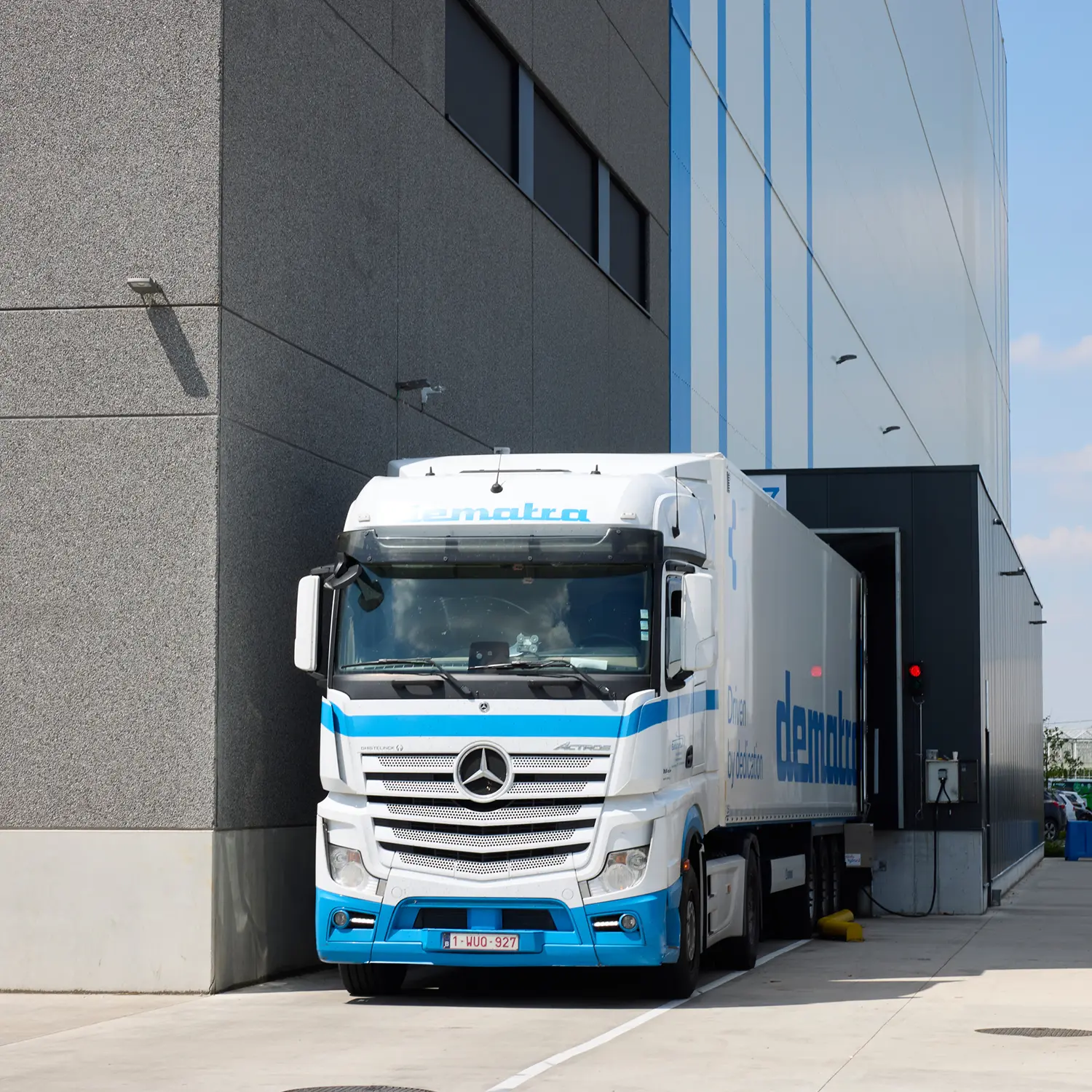 White and blue Mercedes-Benz truck backing into a loading dock of a modern industrial building.