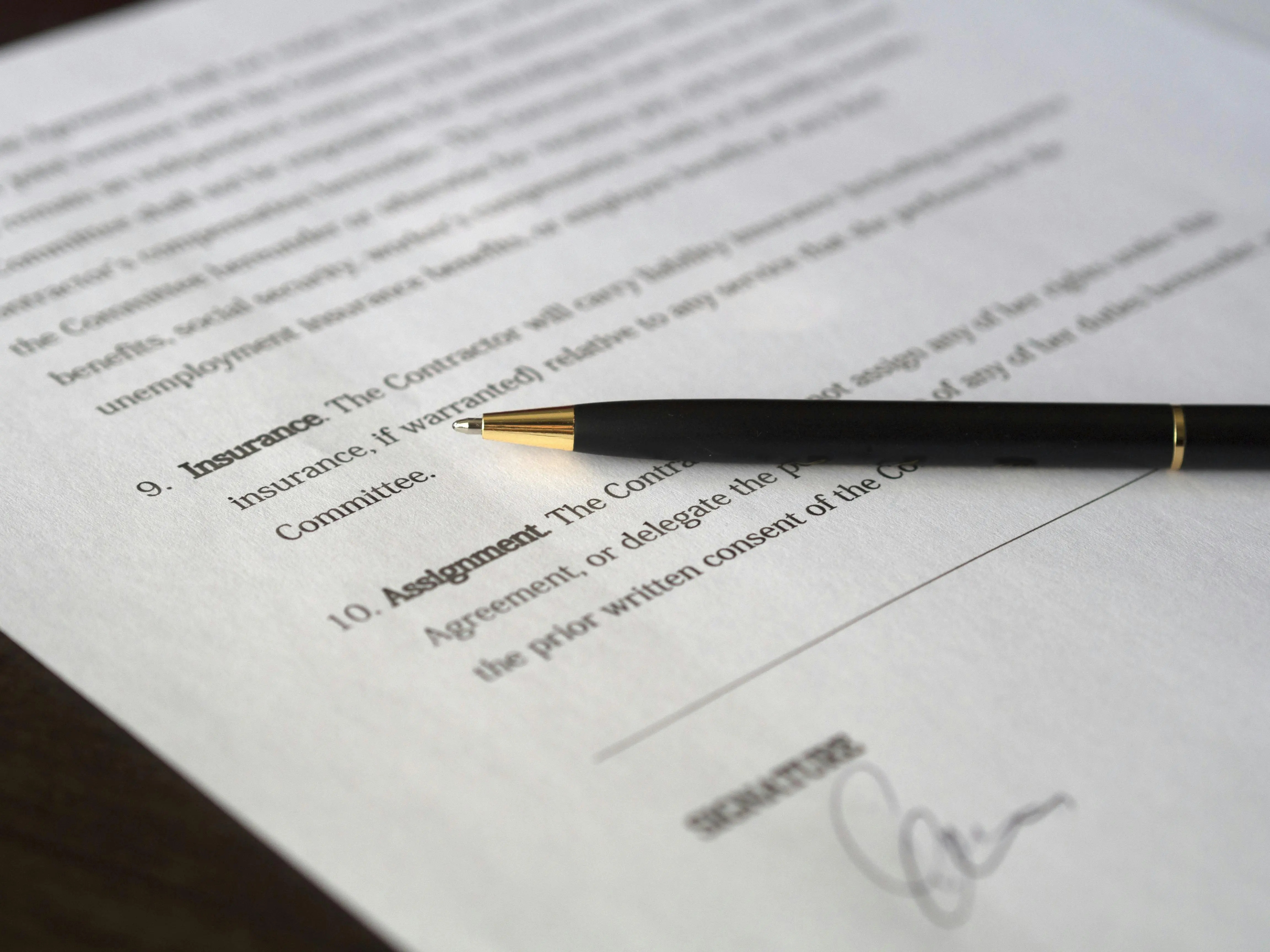 Black pen resting on a contract document with highlighted sections on insurance and assignment, above a handwritten signature.