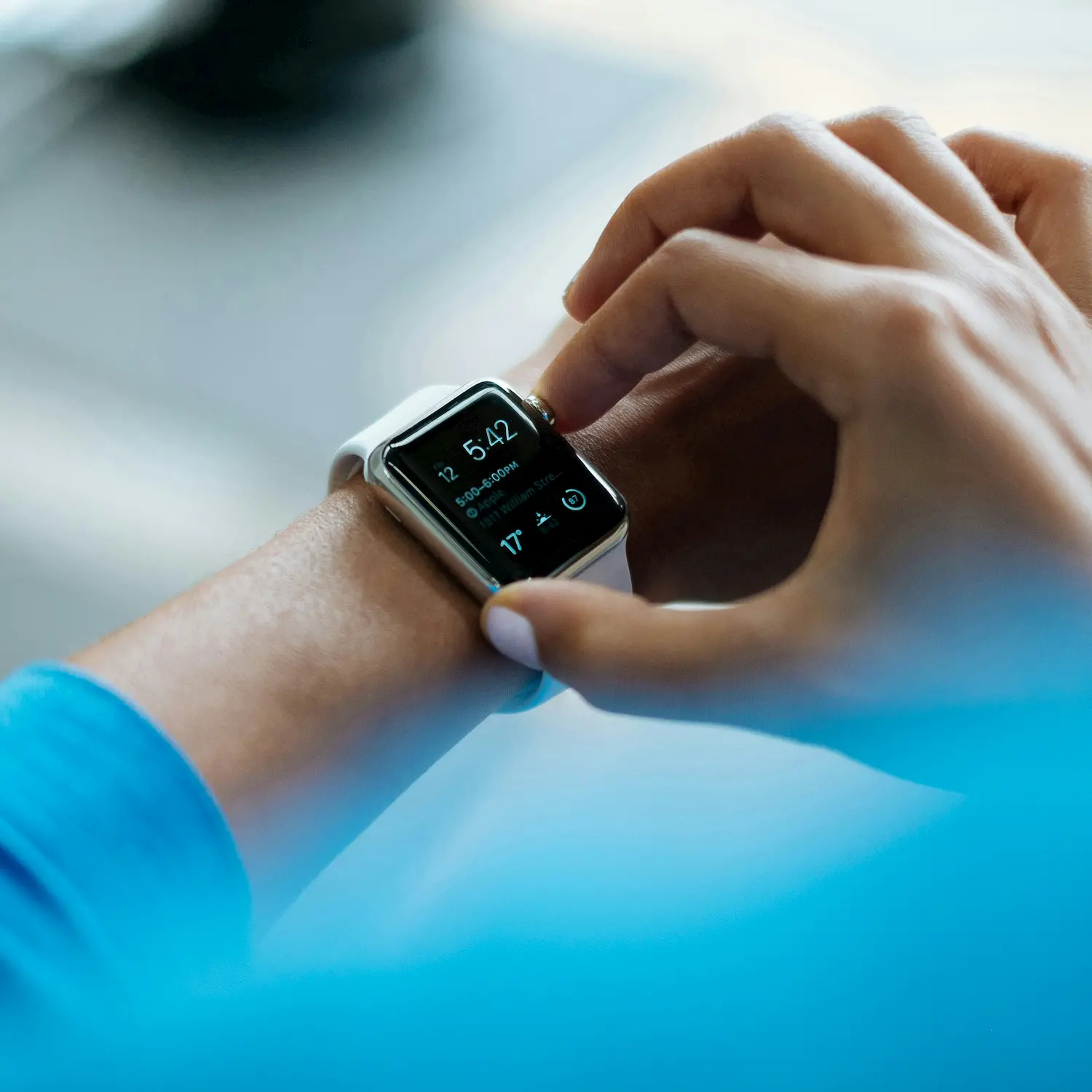 Person adjusting a white smartwatch on their wrist displaying the time and weather.