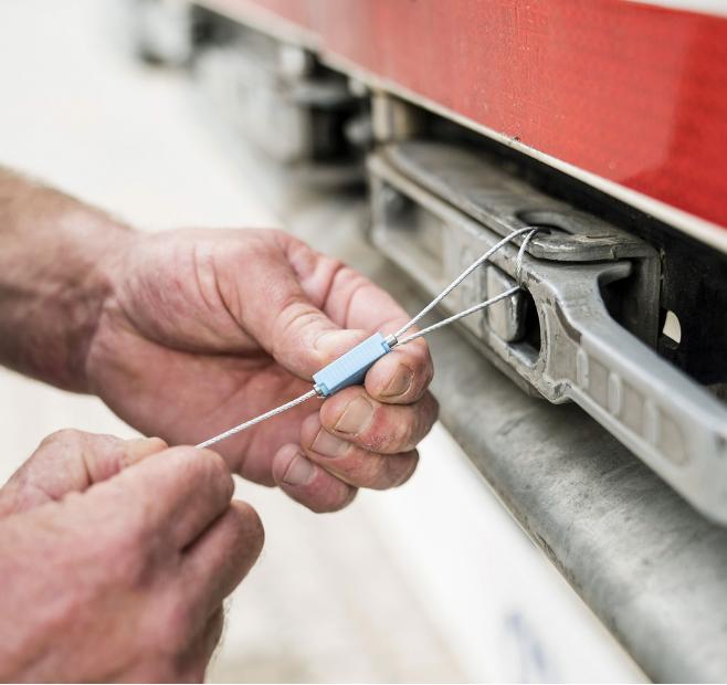 Close-up of hands securing a metal wire seal on a red metal latch.