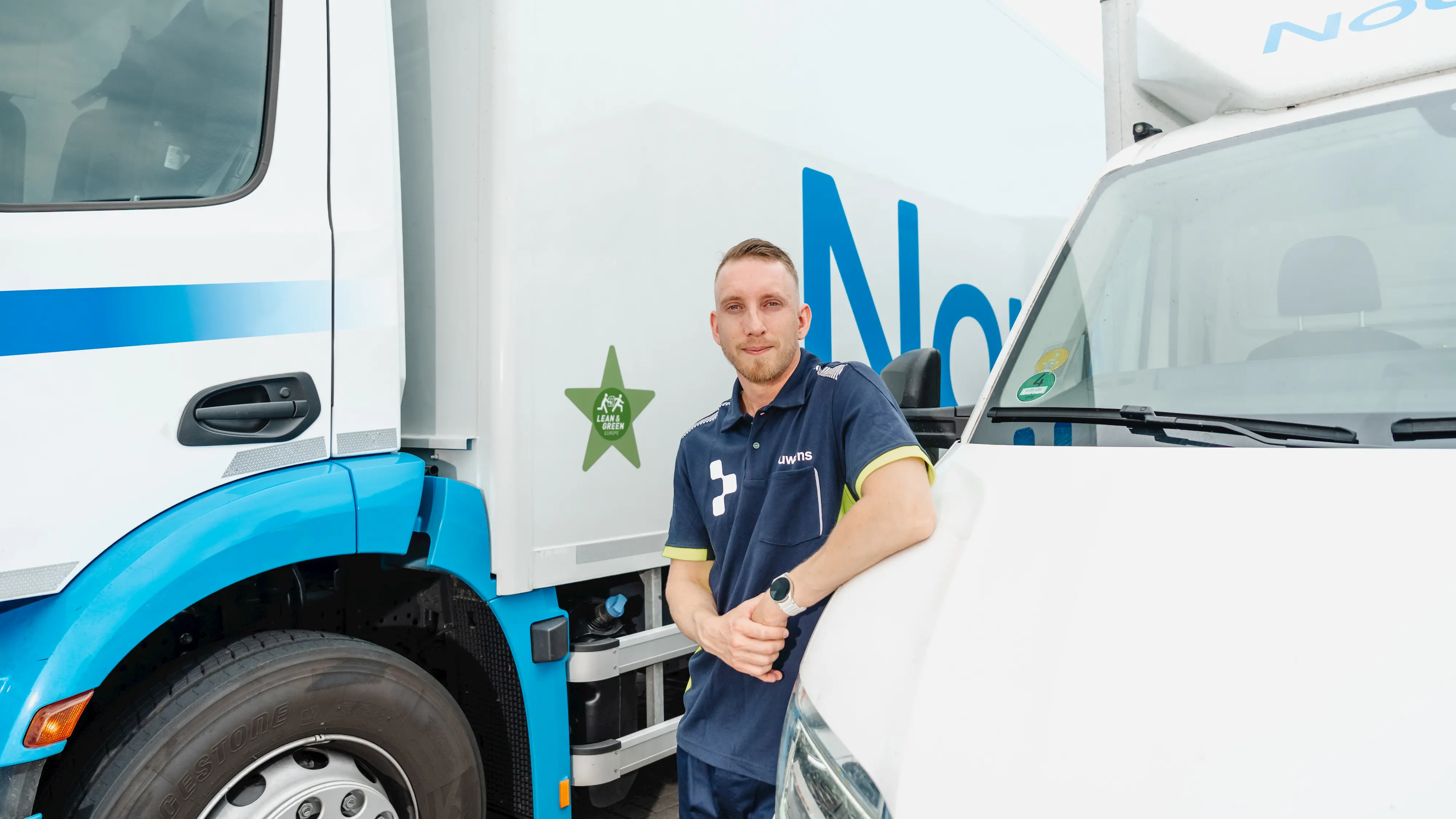 Man in a navy blue uniform leaning on a white delivery truck with a green star logo and blue accents.