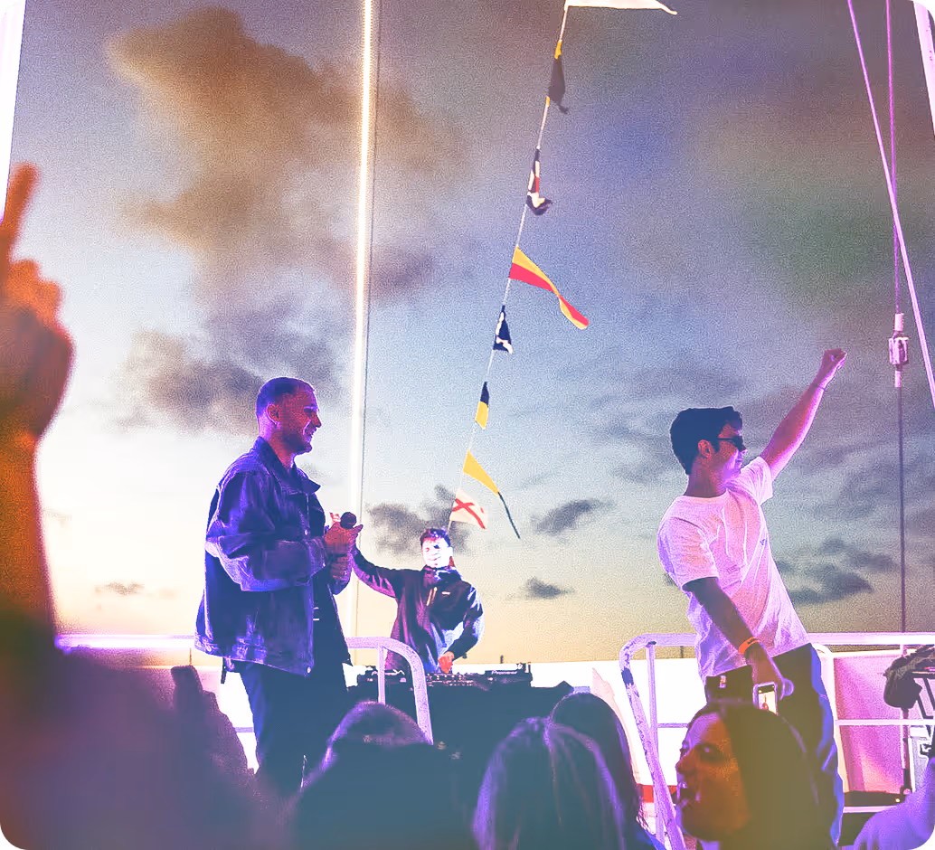 Trois hommes animent une fête en plein air au coucher du soleil, avec un DJ aux platines.