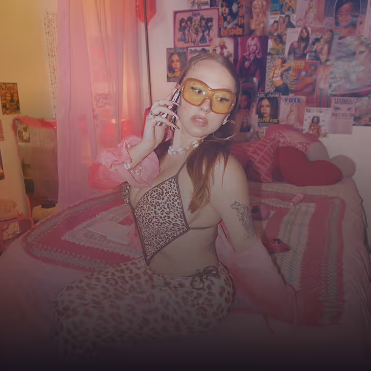 Femme portant des lunettes jaunes et une tenue léopard parlant au téléphone dans une chambre décorée de posters.