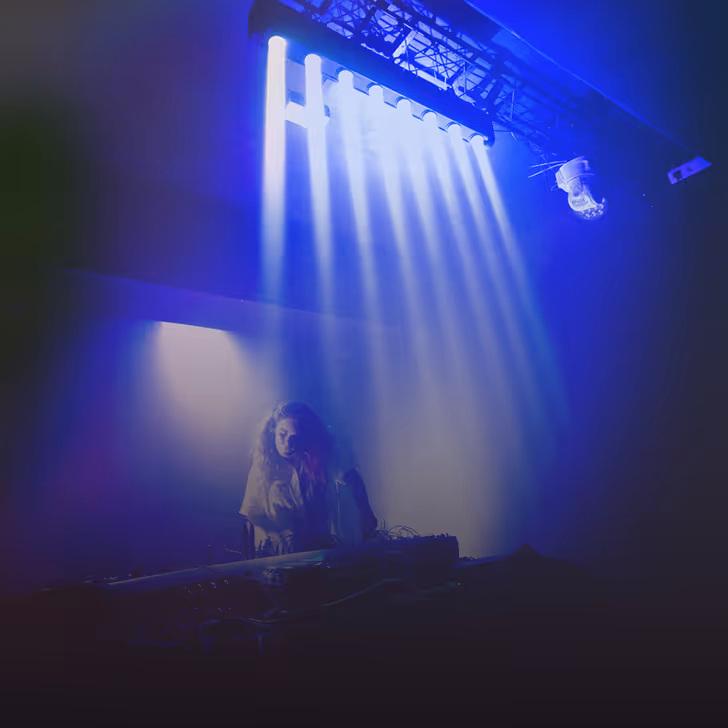 Une DJ joue sous des faisceaux lumineux blancs dans une ambiance sombre et bleutée.