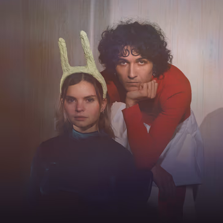 Une femme avec un serre-tête avec des antennes vertes et un homme en pull rouge les regardent sérieusement.