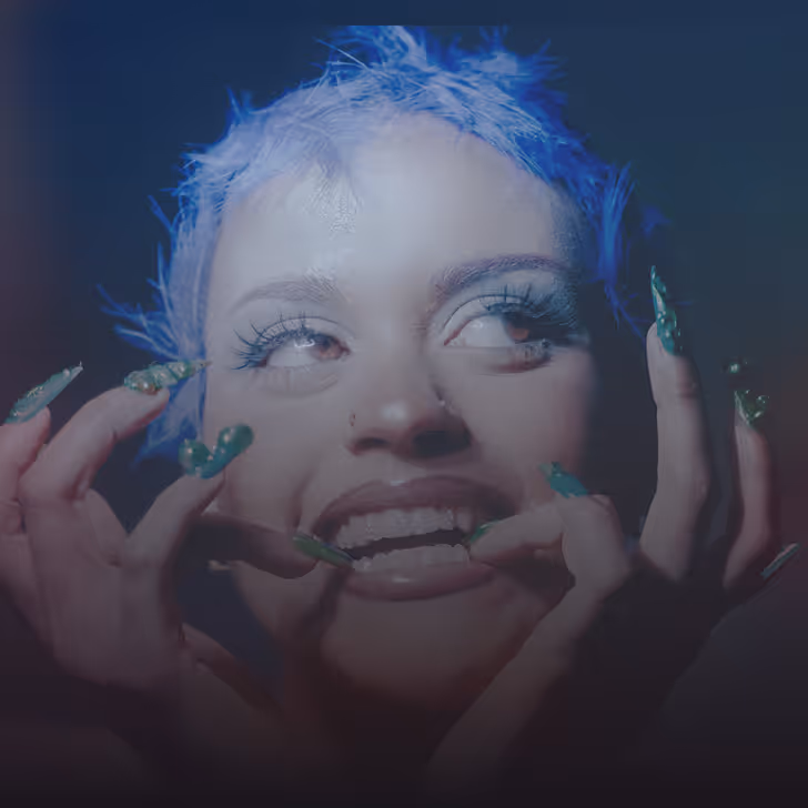 Femme avec cheveux bleus et ongles verts longs faisant une expression faciale expressive.